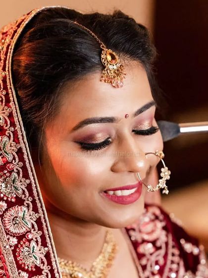 A beautiful North Indian bridal look. The makeup features soft, shimmery rose-gold eyes and a matching red lip, creating a romantic and glowing look for her wedding day.