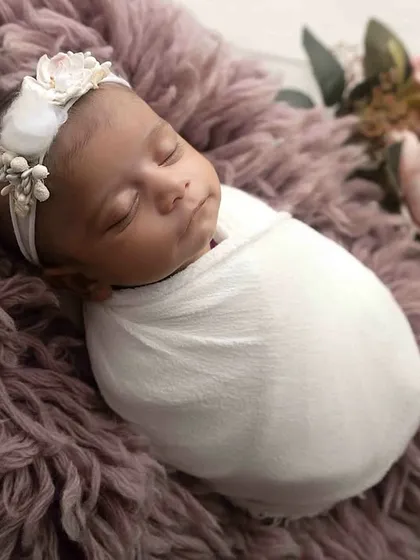 A touch of lavender for this sleeping beauty. Swaddled snugly on a soft, textured rug with delicate flowers, this image showcases a simple yet elegant setup for a newborn girl's portrait.
