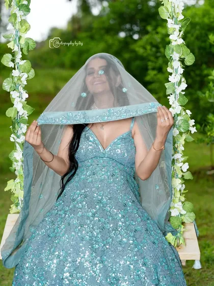 A playful and mysterious shot of a mother-to-be in a sparkling blue gown, peeking from behind a veil on our floral swing.