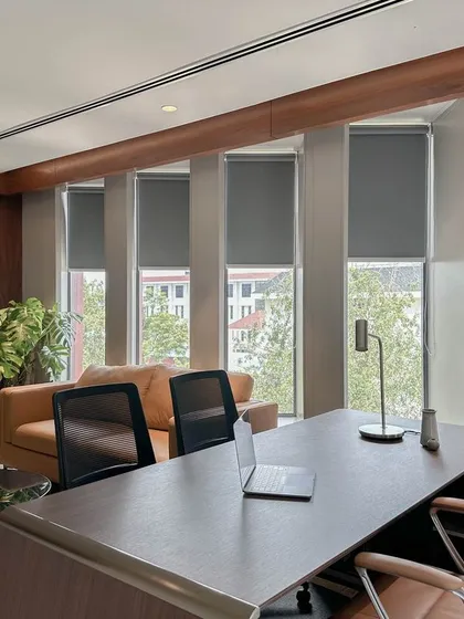 An executive office that combines function with comfort. The space is organized around a large wooden desk and features a dedicated lounge area, custom full-height walnut cabinetry, and large windows with automated blinds for natural light control.