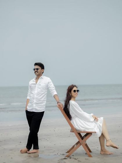 A stylish portrait of a couple on the beach, using simple props like chairs to create a relaxed yet composed photograph.