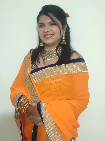 A beautiful Karwa Chauth makeup look. The hair is styled in a simple side-parted look with a touch of volume, letting the festive makeup and orange saree shine.
