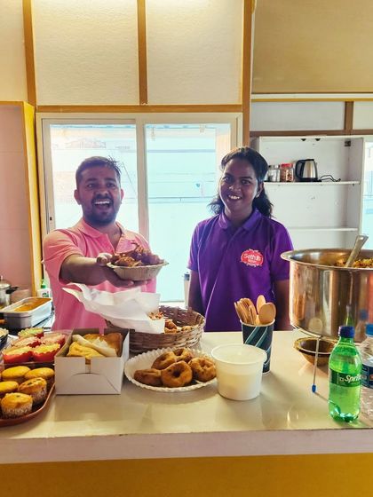 Deepak and a team member proudly presenting a plate of our food. Our counter is stocked with snacks and treats, ready for a busy day.