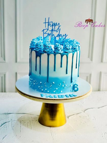 A striking blue ombre drip cake with decorative piping, perfect for a stylish birthday celebration.