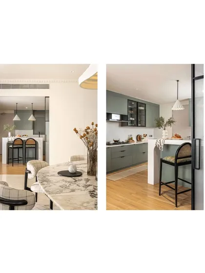 The connection between the dining area and kitchen is both visual and functional. The view from the dining table reveals the soft sage green of the kitchen, while the black-stained wood of the breakfast stools visually ties back to the dining chairs, creating a unified living space.