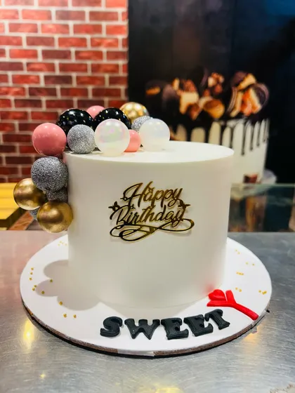 A minimalist white birthday cake with a stylish "Happy Birthday" topper and a modern arrangement of decorative spheres.