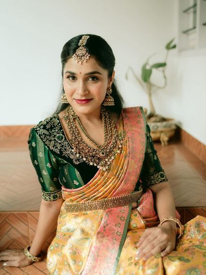 A stunning bridal portrait. The rich yellow and pink saree is paired with an intricately embroidered dark green blouse, creating a look of unmatched elegance.