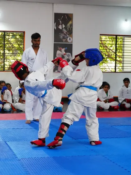 Two of our young students engage in a controlled sparring match during a belt exam, complete with protective gear. We teach competitive karate with a strong emphasis on safety and sportsmanship.