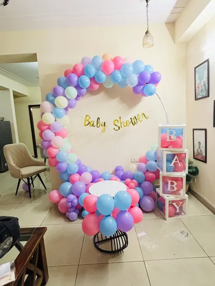 A lovely pastel-themed baby shower decoration with a half-moon circular balloon arch and 'BABY' display boxes.