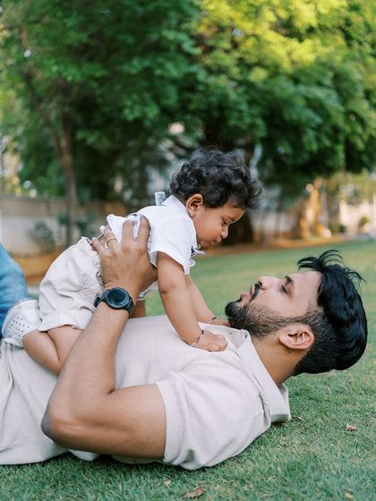 Playful moments like this are the heart of a first birthday shoot. A father lying on the grass, lifting his son up in the air, creating a memory of pure fun.