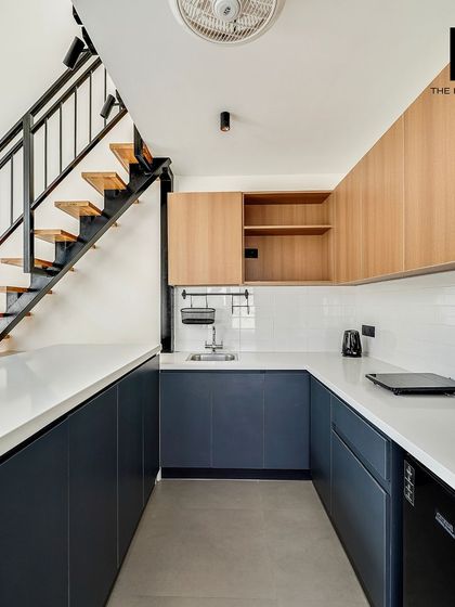 A look at the U-shaped modular kitchen under the mezzanine. The two-tone cabinets in navy and light wood, paired with a white countertop, create a clean and contemporary feel.