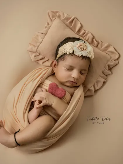 A 20-day-old baby girl, peacefully sleeping while wrapped in a soft peach swaddle. The tiny felt heart she holds adds a touch of sweetness to this classic newborn pose.