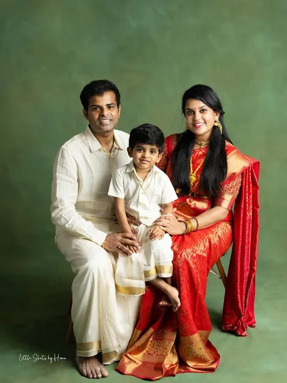 A formal family portrait exuding elegance and warmth. The family is dressed in classic South Indian attire, with the mother in a striking red saree, creating a rich and beautiful image.