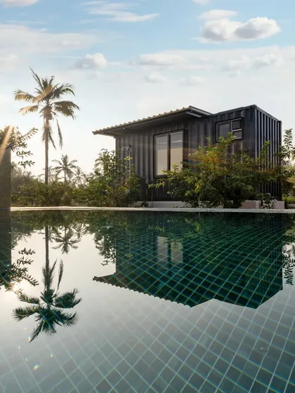A stunning reflection of a container home and a palm tree in the still water of a swimming pool. This artistic shot highlights the project's beautiful design and its serene, tropical location.