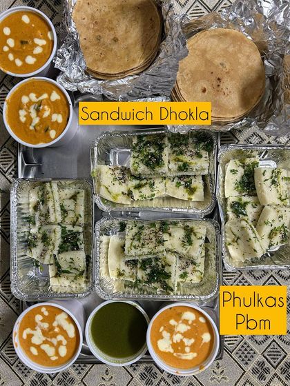 A meal featuring Sandwich Dhokla, Phulkas, and Paneer Butter Masala.