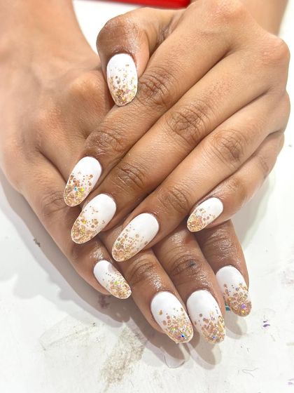 A beautiful white and gold glitter gradient on long almond nails. The glitter is concentrated at the cuticle and fades out, creating an elegant and festive look.