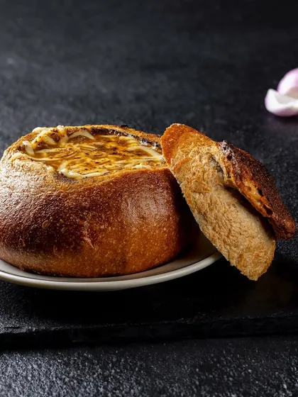 French onion soup served in a bread bowl for PAUL India. The dramatic side lighting highlights the crust of the bread and the melted cheese on top.