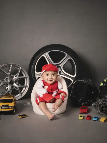 A full view of the 'Biker Baby' setup, featuring a baby boy in a red racing suit surrounded by real car parts, wheels, and toy cars. This is a great example of a highly customized themed session.