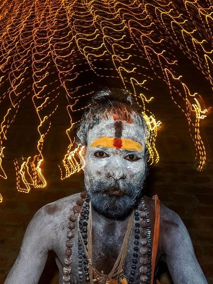 A Naga sadhu stares into the camera with light trails swirling above his head. This creative portrait uses slow shutter speed to capture the mystical energy surrounding him.