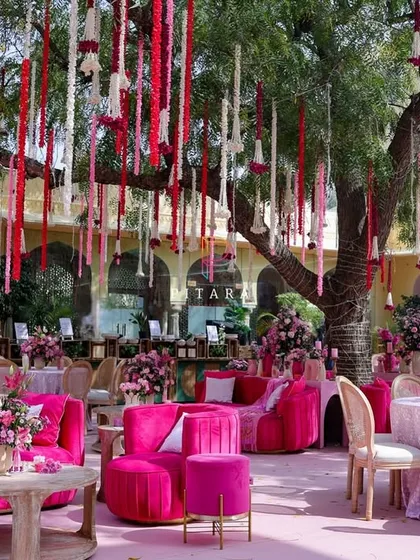 A wider view of the outdoor lounge, showing the mix of velvet sofas and elegant dining tables under the tree with hanging floral tassels. The setup was designed for both relaxation and celebration.