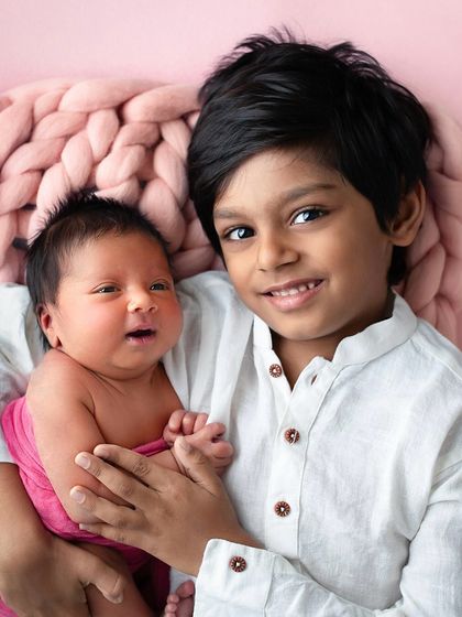 A proud big brother holds his newborn sister, her eyes open and curious. This portrait captures the beginning of a beautiful sibling friendship.