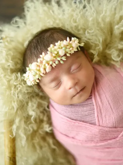 A close-up of a sleeping princess wearing a delicate floral crown and wrapped in a textured pink swaddle.