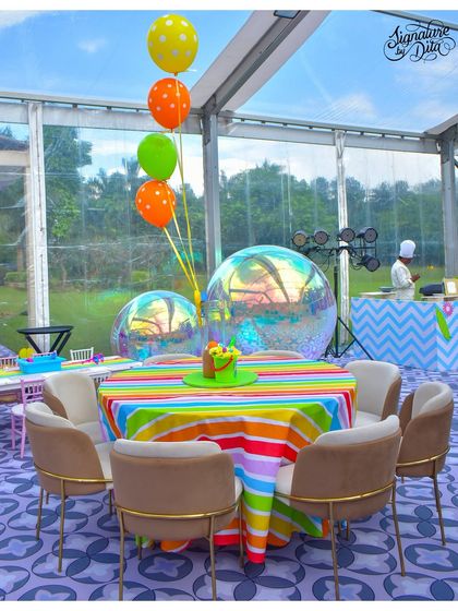 Guest seating at the summer carnival party, held inside a clear-span tent. The tables feature rainbow-striped linens and large, iridescent bubble balloons that catch the light beautifully.