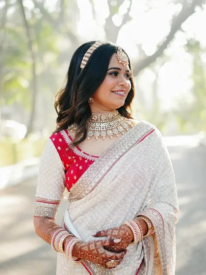 A close-up portrait of the bride in a beautiful white and red saree. The soft morning light illuminates her features and the intricate details of her jewelry.