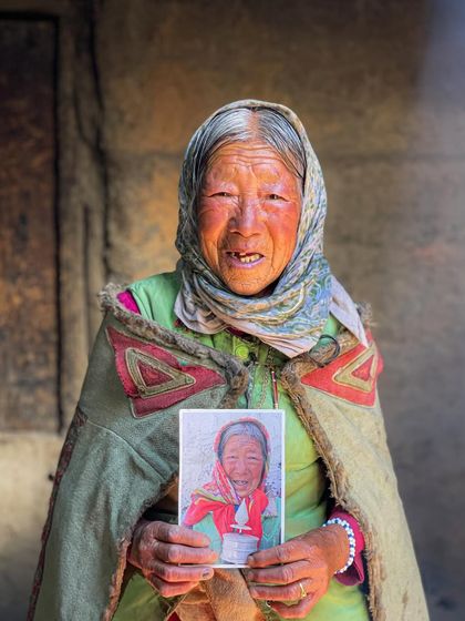 A beautiful, emotional portrait of Eve Yang Chew from Hikkim village holding a photo from her youth. Her expression is full of nostalgia and the weight of a life lived.