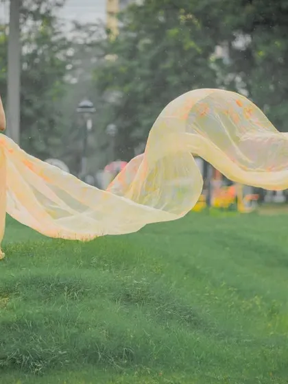 A wide shot showing the beautiful, wind-swept train of this yellow and pink gown in a green park.