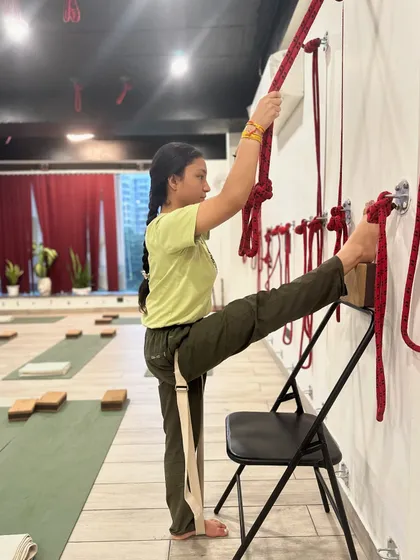 Alignment is everything. In this supported leg stretch, the student uses a chair, ropes, and a belt to work on hamstring flexibility while maintaining a stable pelvis. This precision ensures the stretch is effective and safe for the joints.