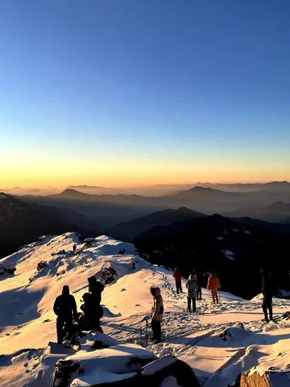 Trekkers at the Kedarkantha summit during sunrise, with layers of Himalayan peaks in the background. This is the reward for an early morning start and a challenging climb.