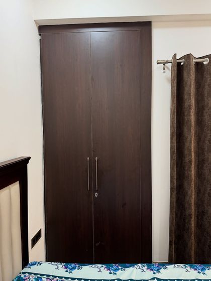 A simple yet elegant dark wood finish wardrobe, providing a classic look and ample storage for a bedroom in a 2BHK apartment.