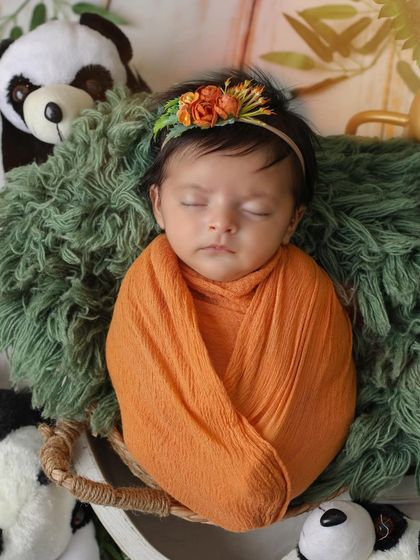 A close-up of our little panda, sleeping peacefully. The details, like the floral headband and soft green textures, make this animal-themed newborn shoot extra special.
