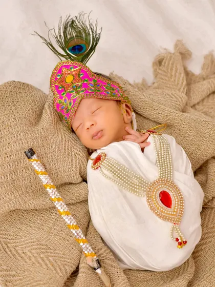 A newborn peacefully sleeps dressed as Little Krishna, complete with a tiny flute and peacock feather. This themed shoot combines cultural tradition with the serene innocence of a newborn.