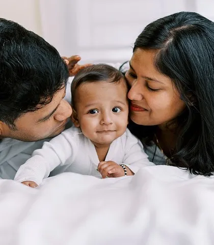 A family portrait from the same six-month session, with both parents kissing their happy baby.