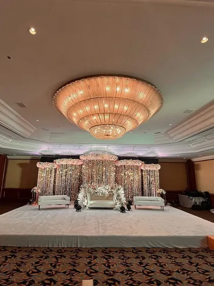 This image shows the grand scale of a reception setup inside a hotel ballroom. The glittering stage is the focal point, complemented by the hall's magnificent chandelier.