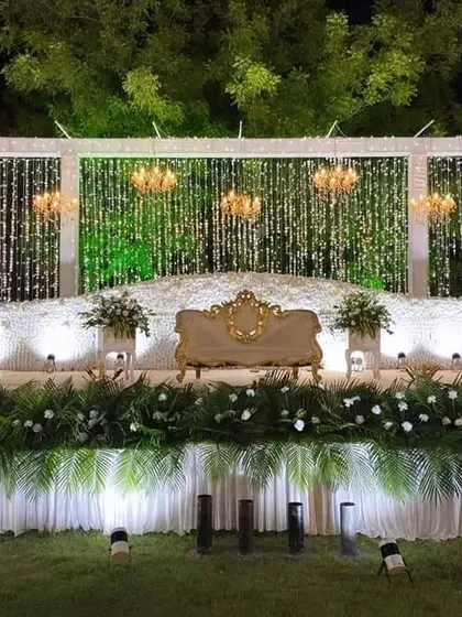 For this outdoor reception, I designed an elegant stage featuring cascading crystal strings, grand chandeliers, and a lush base of white flowers and greenery, creating a magical ambiance under the open sky.