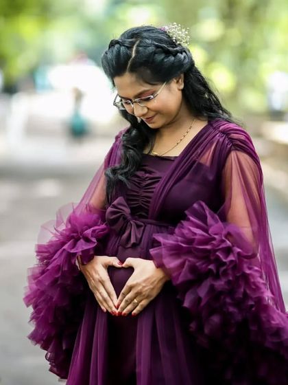A close-up look at the heart you're creating. This mom-to-be makes a heart shape on her belly, showing off the delicate ruffled sleeves of the purple gown. It's these small, tender moments that make a maternity shoot so special.