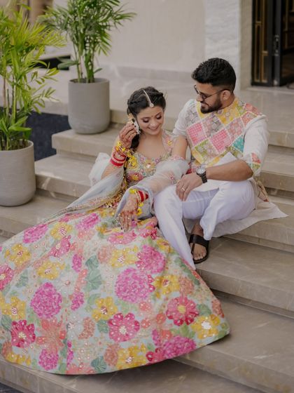 A sweet moment on the steps, the bride adjusting her bangles while the groom looks on with affection.