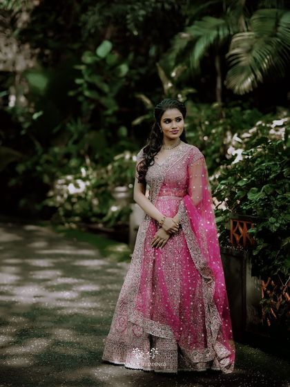 The bride-to-be in her beautiful pink and silver lehenga, posing in a garden setting with a look of serene happiness.