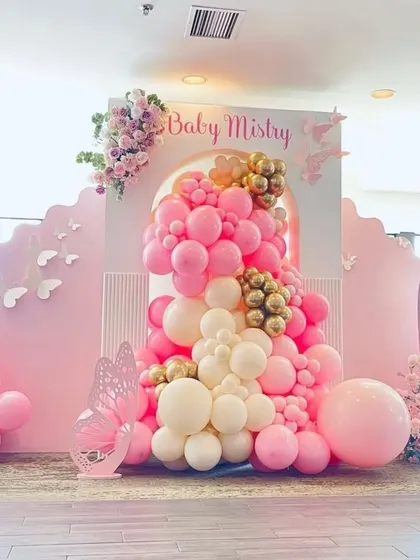 A pretty in pink butterfly-themed baby shower backdrop, featuring a cascade of pink and gold balloons and delicate butterfly cutouts.