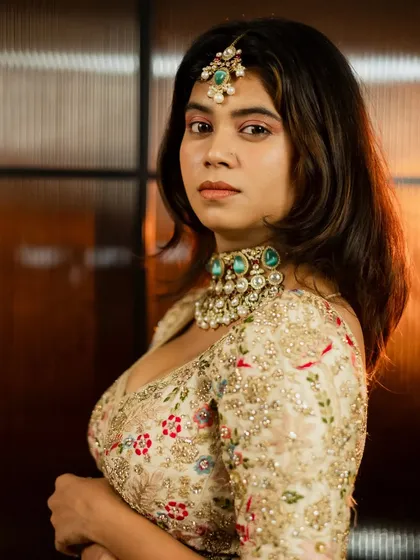 A confident bridal portrait. The model's pose highlights the intricate details of her designer lehenga and choker necklace, with warm backlighting adding a touch of glamour.