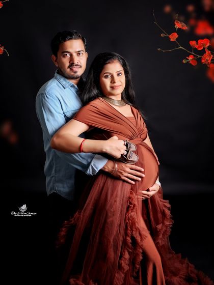 The couple holds a pair of tiny baby shoes together over the bump. This close-up shot against a dark background is full of emotion and anticipation.