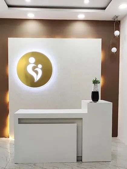 The reception area for Momfirst, a wellness clinic. The design uses clean lines, a calm color palette, and focused lighting on the brand's logo to create a welcoming, professional, and reassuring environment for visitors.