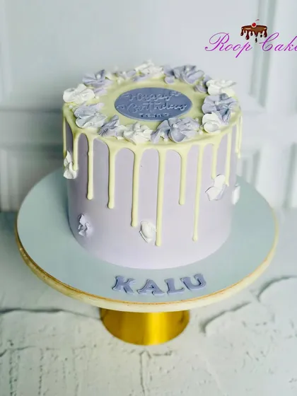 A beautiful lavender drip cake with white chocolate drips and delicate floral piping on top.