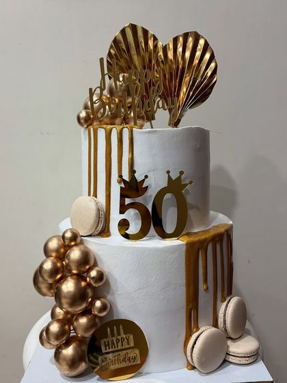 A closer look at the elegant two-tier 50th birthday cake. The combination of white, gold, and macarons creates a truly luxurious feel.