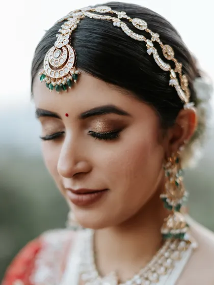 The beauty is in the details. A flawless bridal bun provides the perfect canvas for this stunning matha patti, creating a look of pure elegance with soft, shimmering eye makeup.