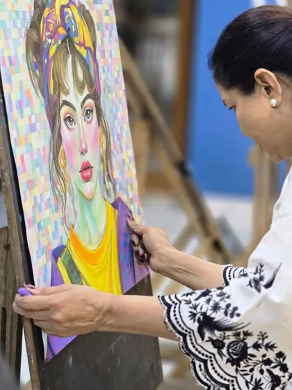An artist carefully places her colorful oil pastel portrait on an easel, a piece defined by its vibrant palette and a unique pixelated background.