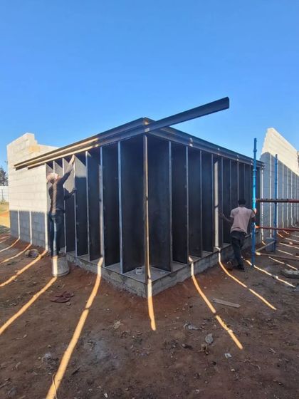 Workers install the structural framework of the gallery. The morning light casts long shadows, highlighting the rhythm of the vertical fins that will define the building's facade.